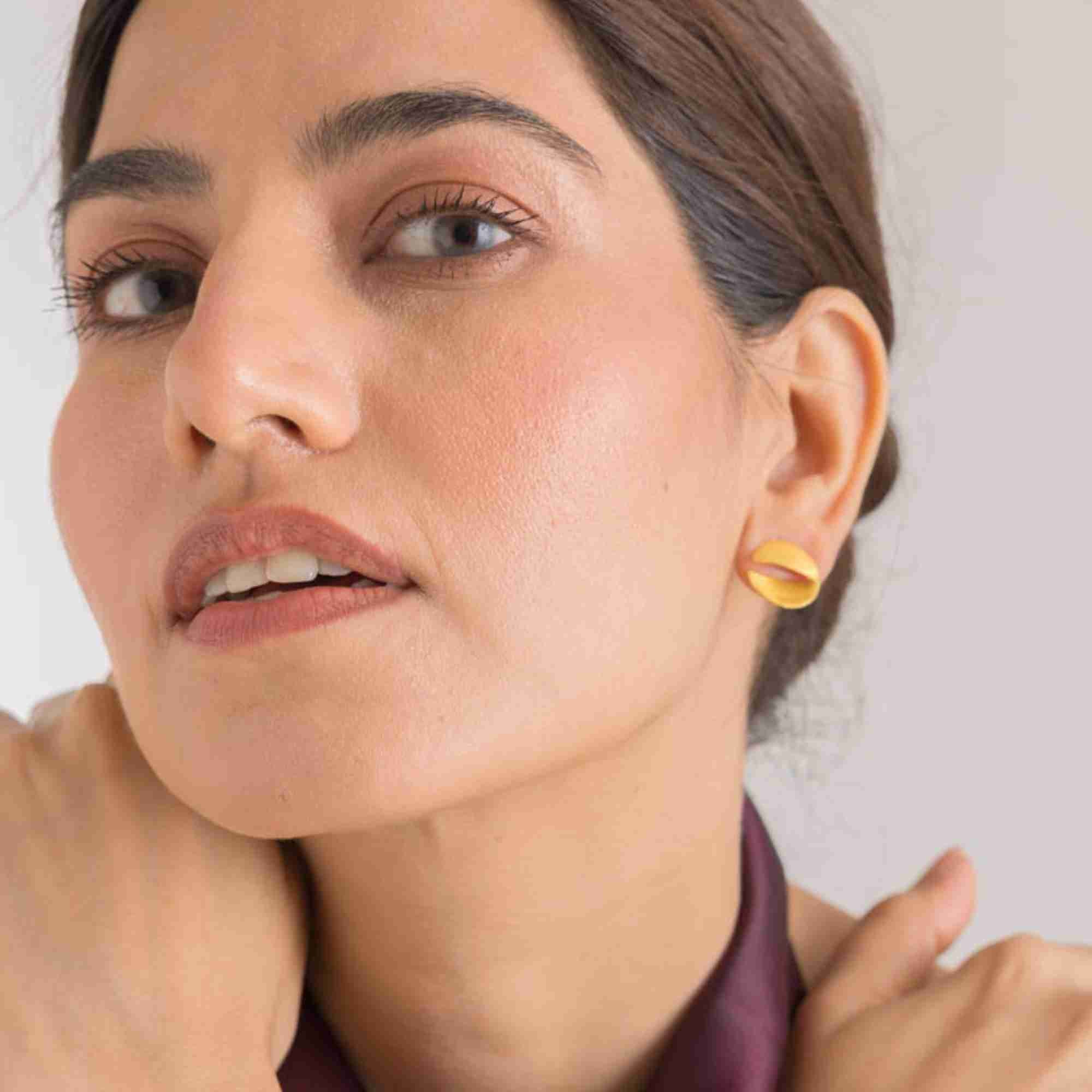 Front-angled portrait of a model styled with the gold Shimmering Disks Sculptural Disc Stud Earrings.