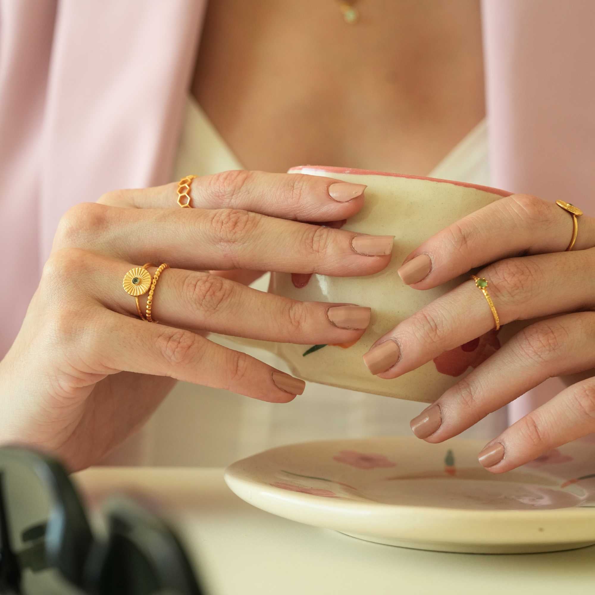 Lifestyle shot of a model cradling a ceramic mug with both hands, showcasing a curated collection of gold jewelry featuring the Delicate Vintage Beaded Stacking Ring Gold on her right hand, by Protsaah Zurich.