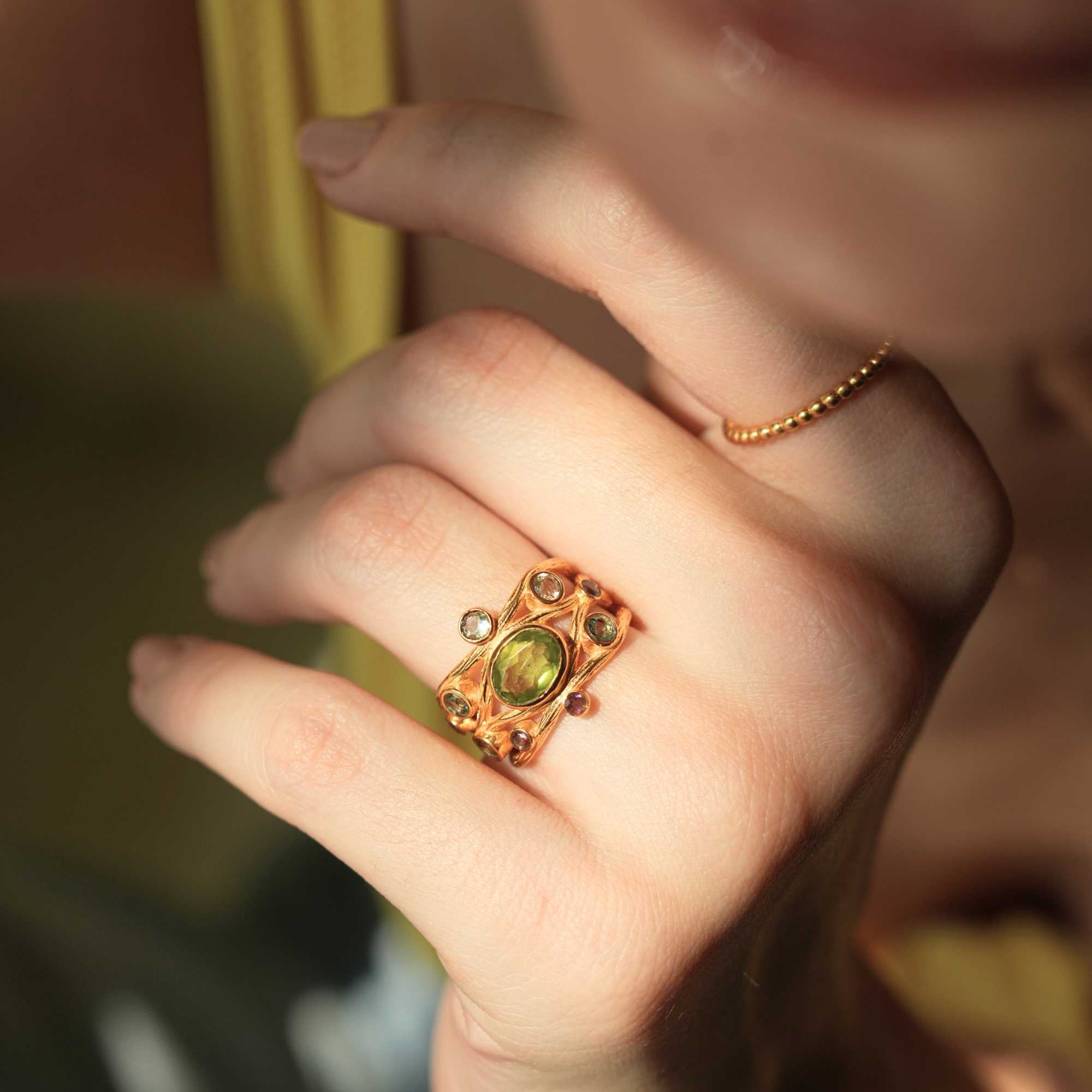 Close-up lifestyle view of a model resting her chin on her hand, showing the Delicate Vintage Beaded Stacking Ring Gold stacked discretely on her index finger while a statement green gemstone ring adorns her ring finger, by Protsaah Zurich.