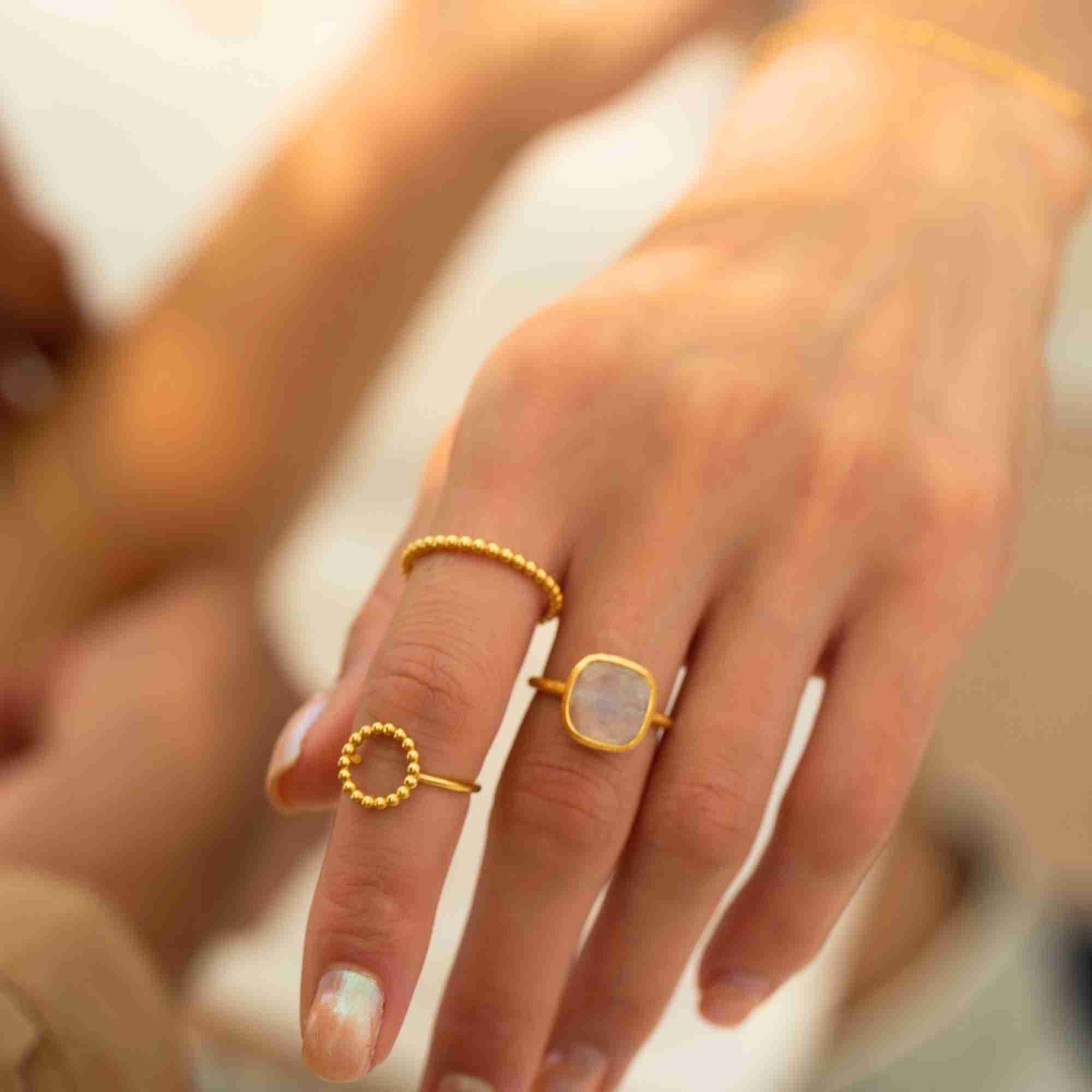 Close-up lifestyle portrait named Delicate Vintage showcasing a minimalist gold ring curation on a model's hand. Worn at the base of the index finger is the Delicate Vintage Beaded Stacking Ring Gold, featuring a slender, continuous bubble-bead texture crafted from premium 22K gold vermeil, beautifully paired with a square moonstone ring and an open-circle beaded ring by Protsaah Zurich.