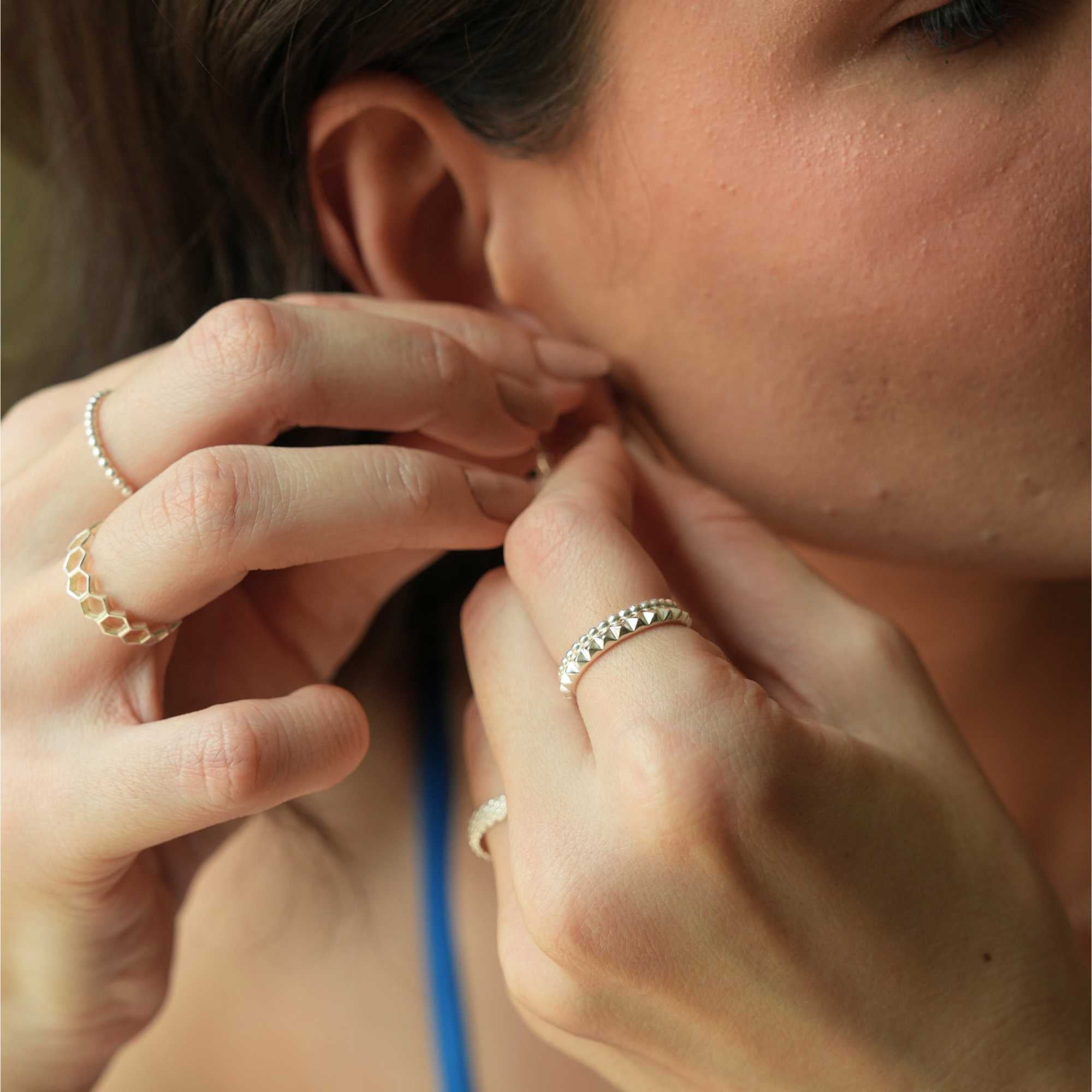 Close-up lifestyle view of a model's hands as she adjusts her earring, showing a multi-ring style combination that highlights the Delicate Vintage Beaded Stacking Ring Silver, by Protsaah Zurich.