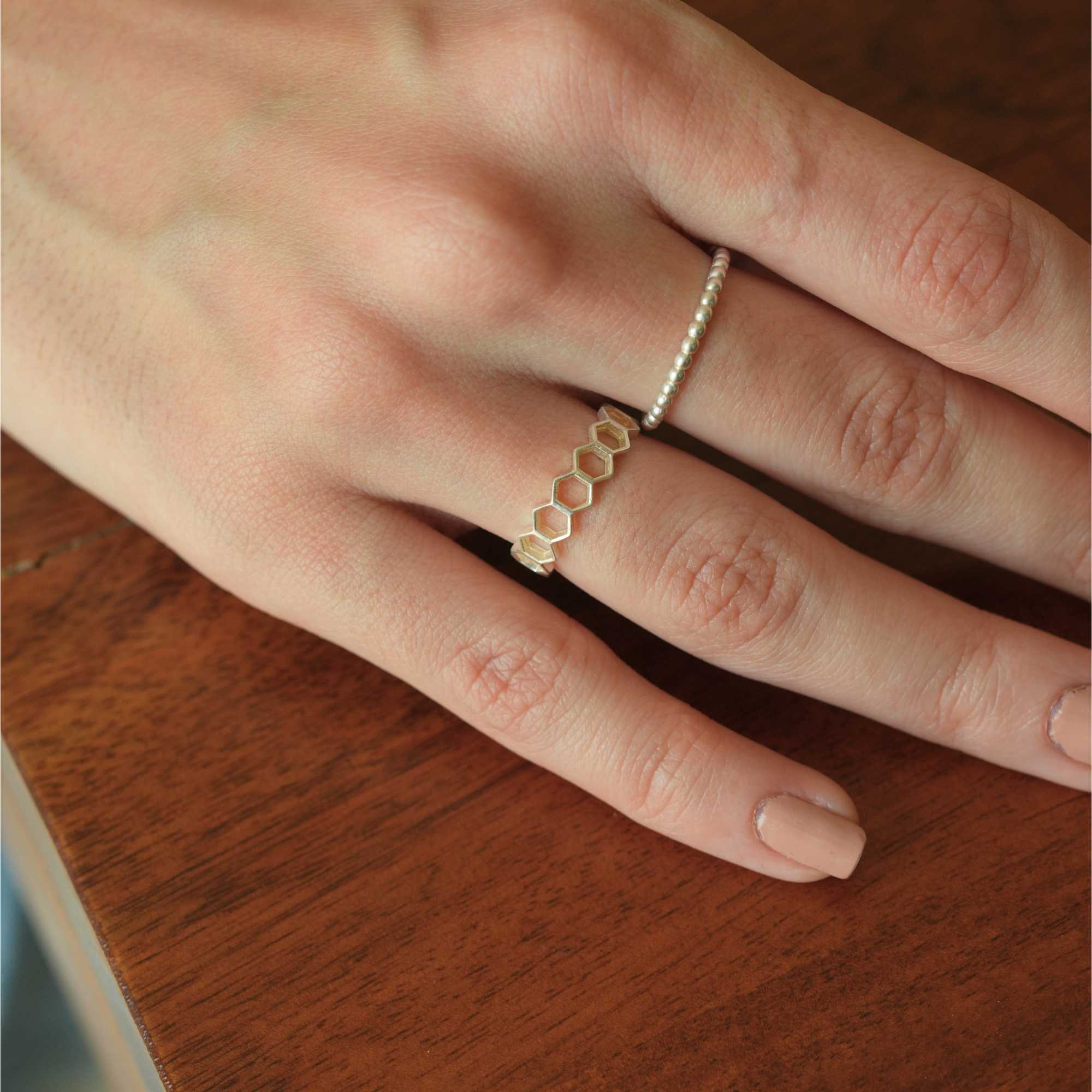 Elegant lifestyle close-up of a model's hand resting on a rich wooden surface, displaying the subtle metallic textures of the Delicate Vintage Beaded Stacking Ring Silver alongside a honeycomb pattern ring, by Protsaah Zurich.