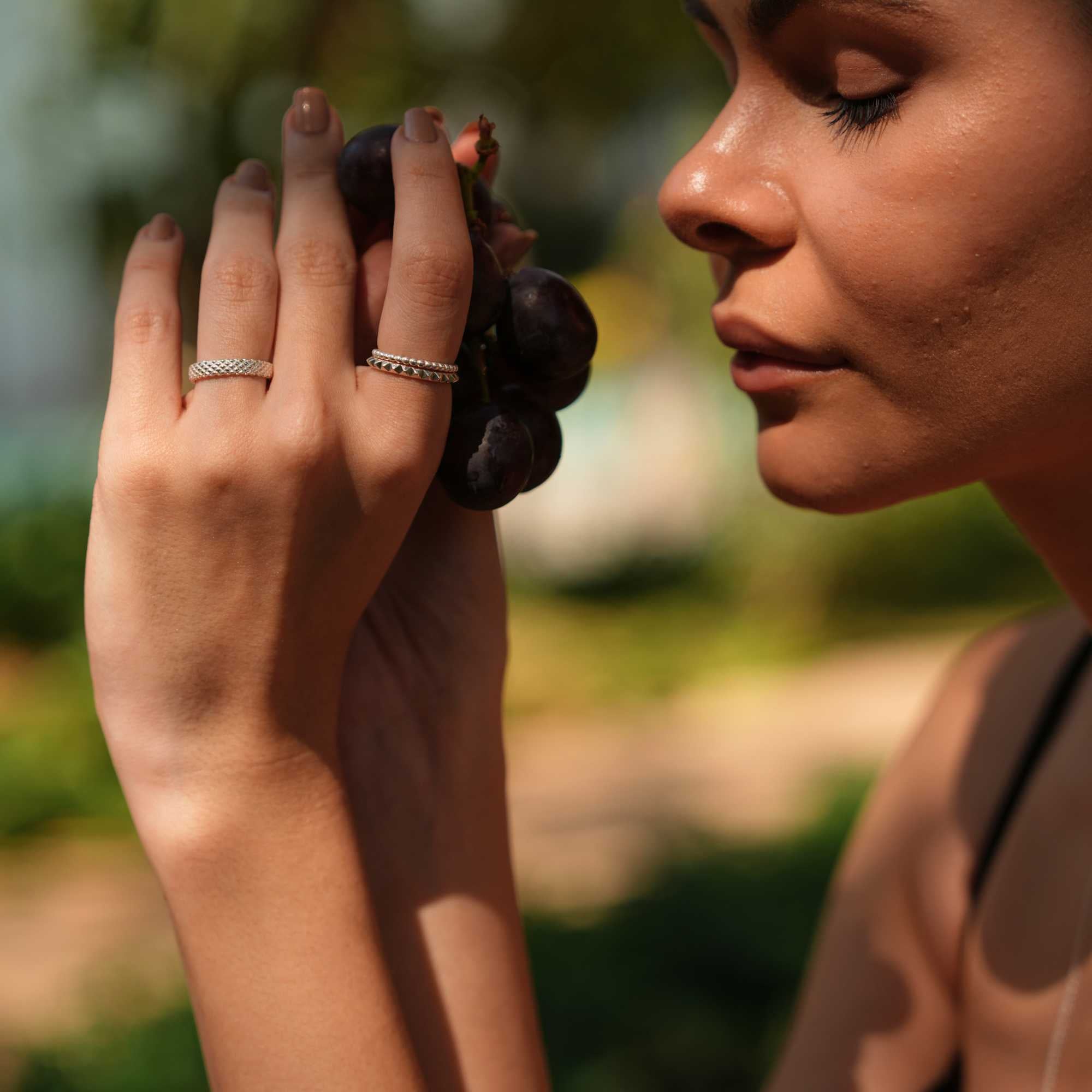 Sunlit lifestyle view of a model lying on green grass, wearing delicate layered silver necklaces while her hand with the Delicate Vintage Beaded Stacking Ring Silver rests in the foreground, by Protsaah Zurich.