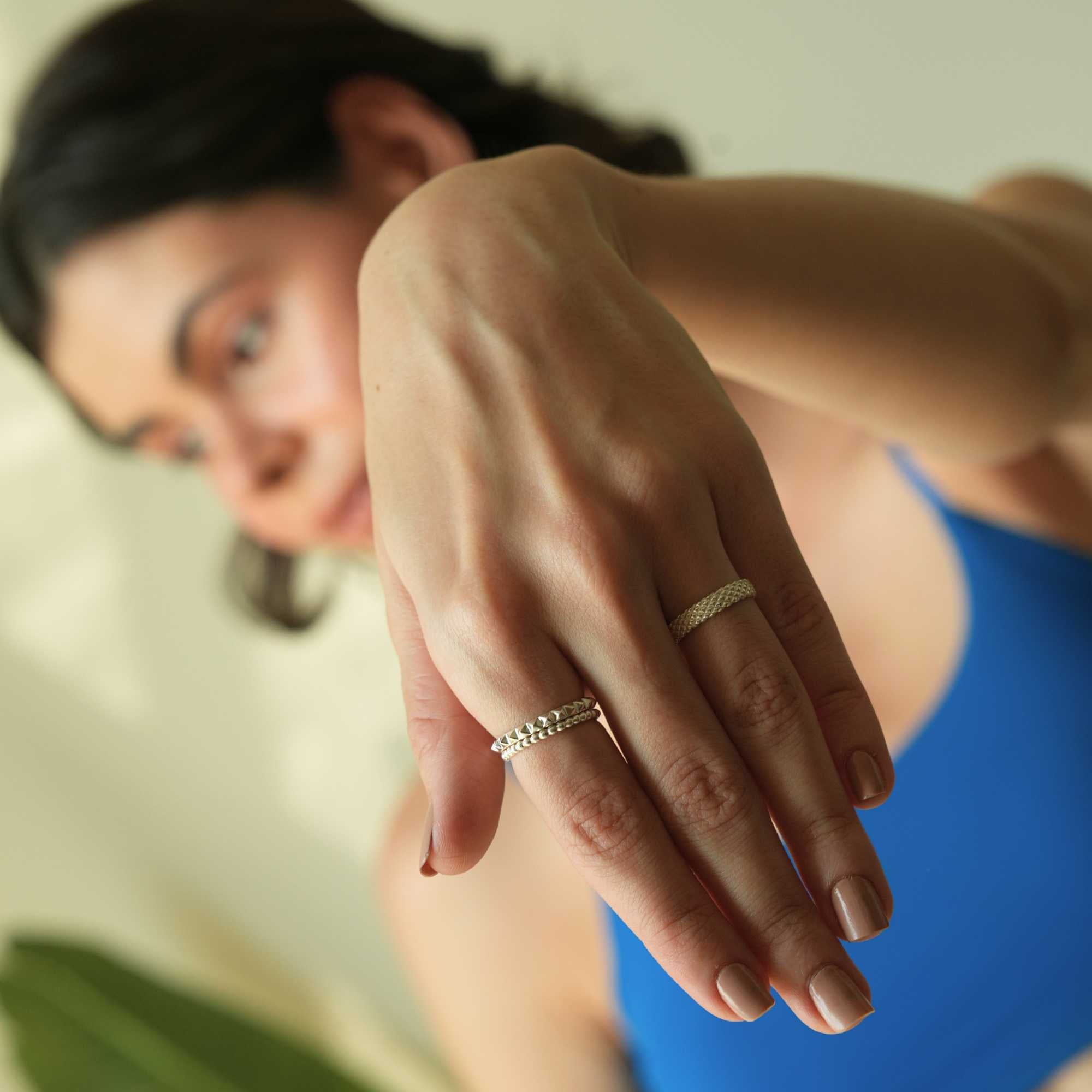 Lifestyle portrait with a soft out-of-focus model in the background, focusing forward on her hand wearing a textured silver band combination featuring the Delicate Vintage Beaded Stacking Ring Silver, by Protsaah Zurich.