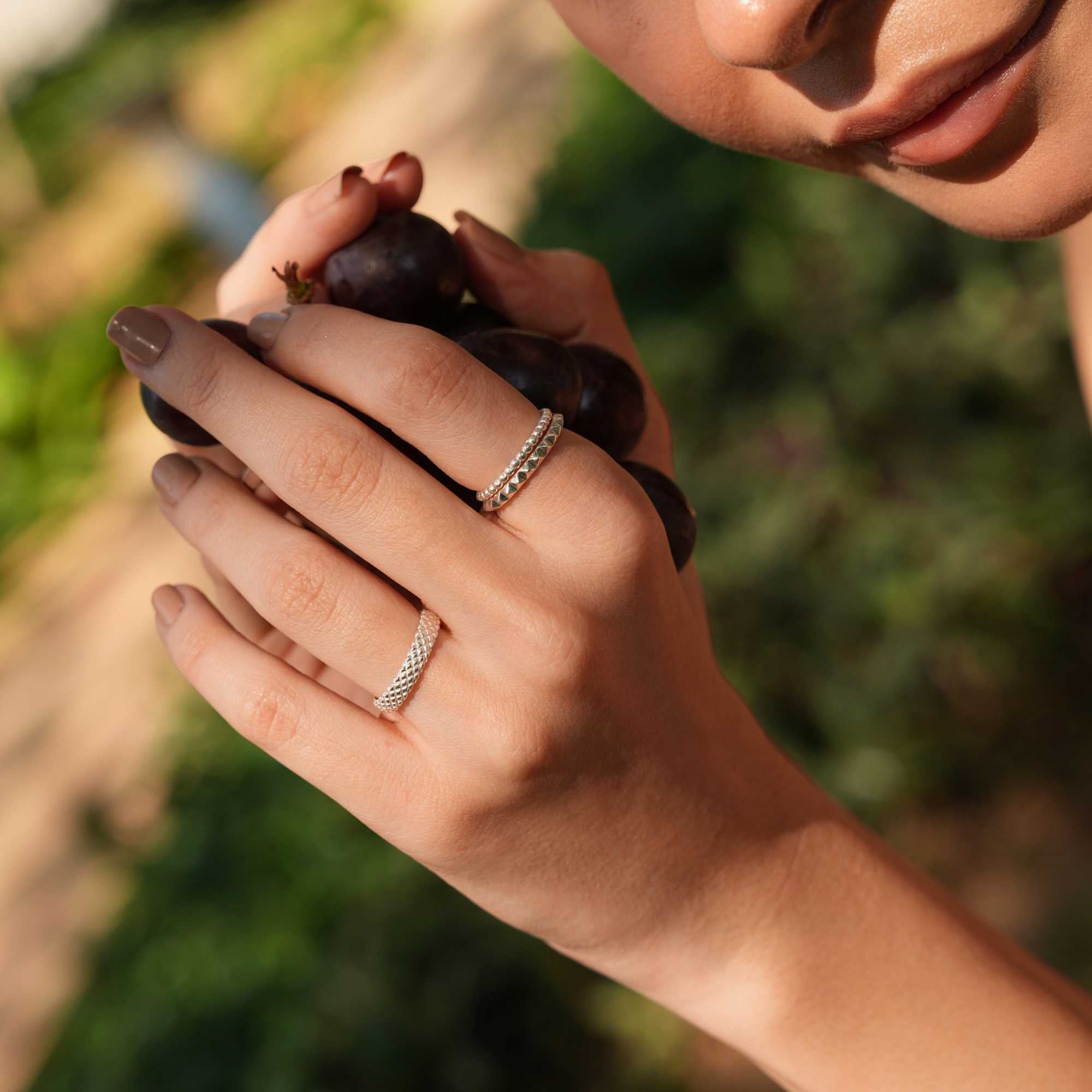 Soft-focus lifestyle portrait of a model looking down while holding grapes, showing the sparkle of her silver stacking rings, including the Delicate Vintage Beaded Stacking Ring Silver, by Protsaah Zurich.