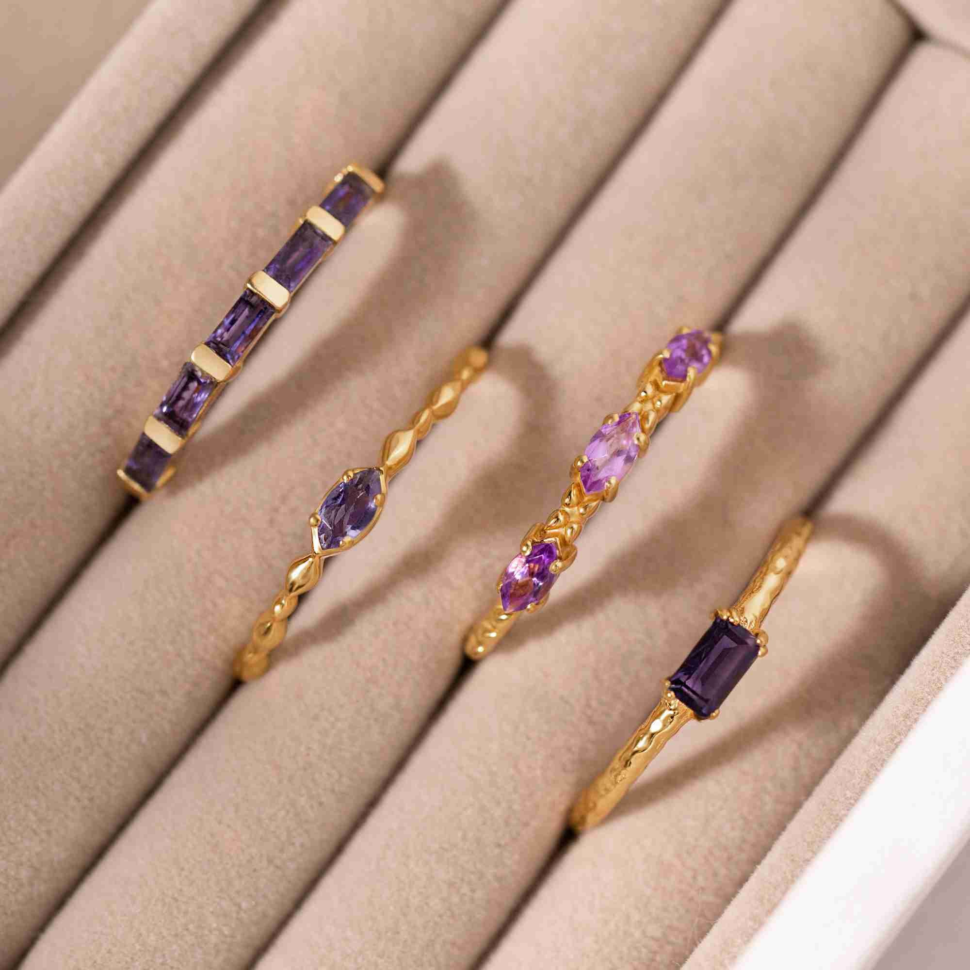 Lifestyle flatlay picture named Delicate Vintage displaying a collection of purple and blue gemstone rings in a velvet jewelry box drawer. Featured prominently is a dainty 22K gold vermeil ring with a single, slender marquise-cut natural blue gemstone set horizontally on a delicate beaded-style band by Protsaah Zurich.