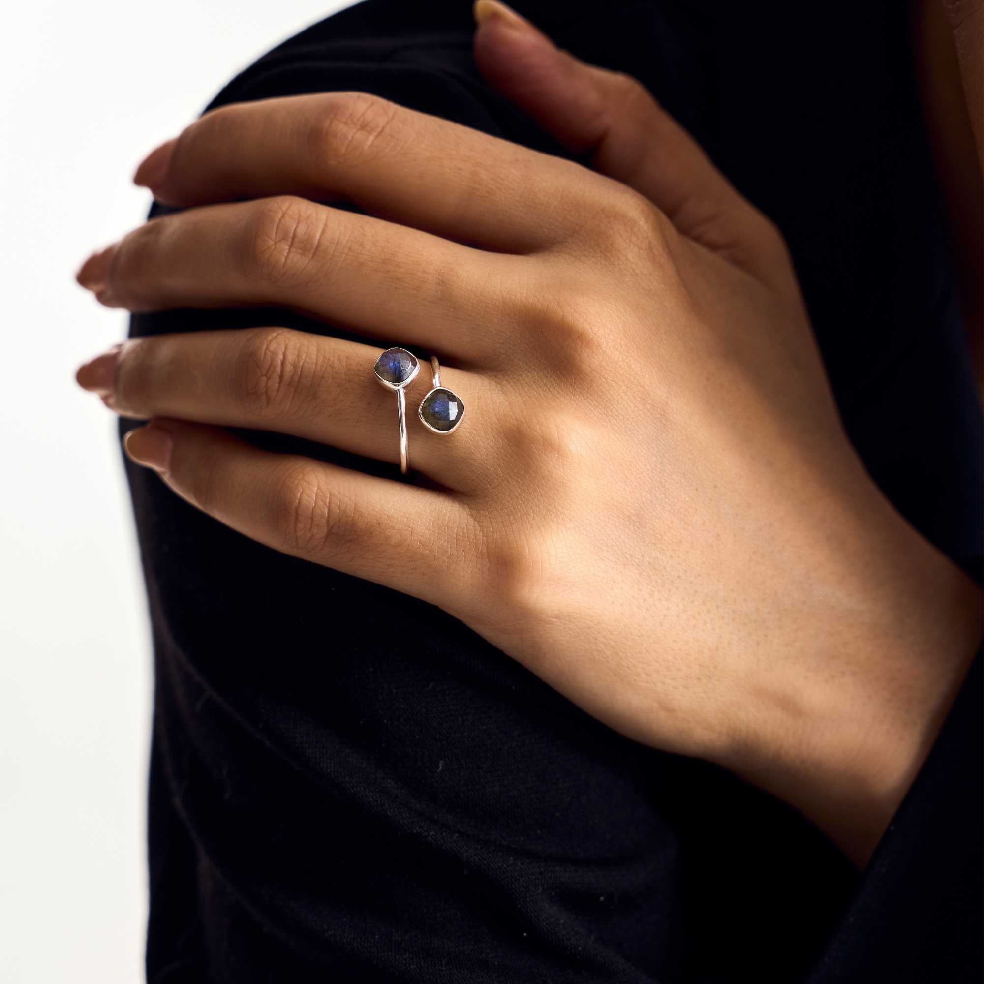 Close-up lifestyle portrait focusing on a model's hand against her shoulder, highlighting the Geo Glam Toi et Moi Labradorite Ring Gold, referencing file name 52.jpg. The lighting is adjusted to capture the intense blue and grey iridescence within the dual cushion-like bezel-set labradorite gemstones.