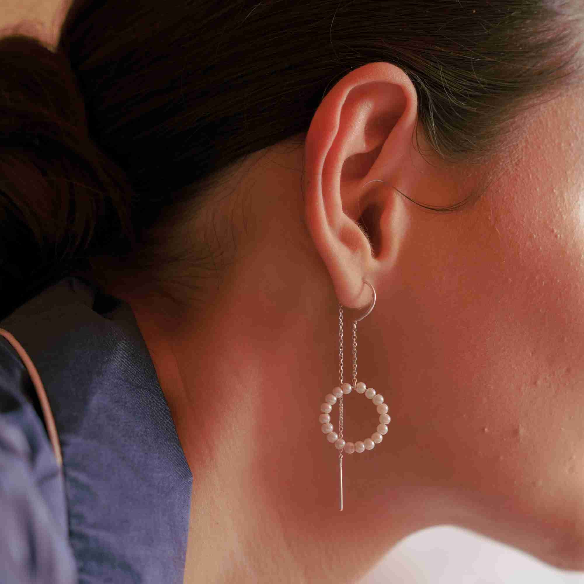 Close-up lifestyle view focusing on the ear and neckline of a model wearing the PEARLS GALORE Seed Pearl Circle Chain Threader Earrings Silver, referencing file name Pearl_Galore_11.jpg. The image captures the fine detail of the sterling silver threader bar and the elegant contrast between the sleek metallic chain and the organic texture of the seed pearl circle.