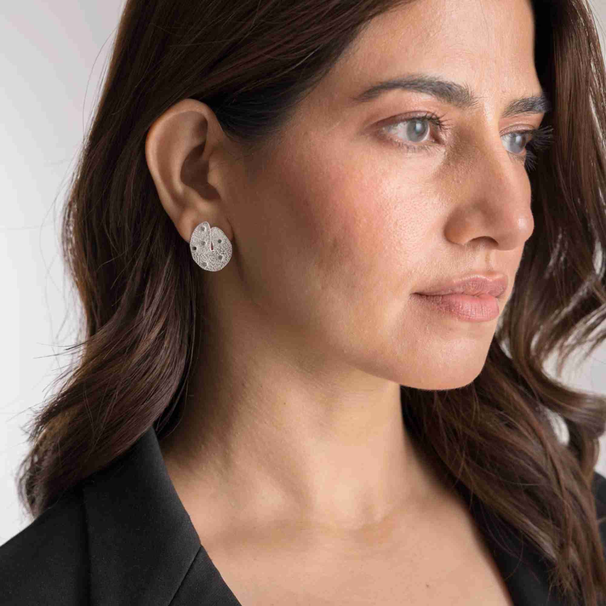 Side profile lifestyle model image displaying the Ribbons and Lace Galaxy Multi-Gemstone Stud Earrings Silver, referencing file name Ribbon_Lace_17_2eb6576a-d063-4e3c-a924-88d9749bd85c.jpg. This view highlights the flat yet dimensional fit of the textured silver galaxy cluster stud earring against the ear lobe, paired elegantly with casual corporate attire.