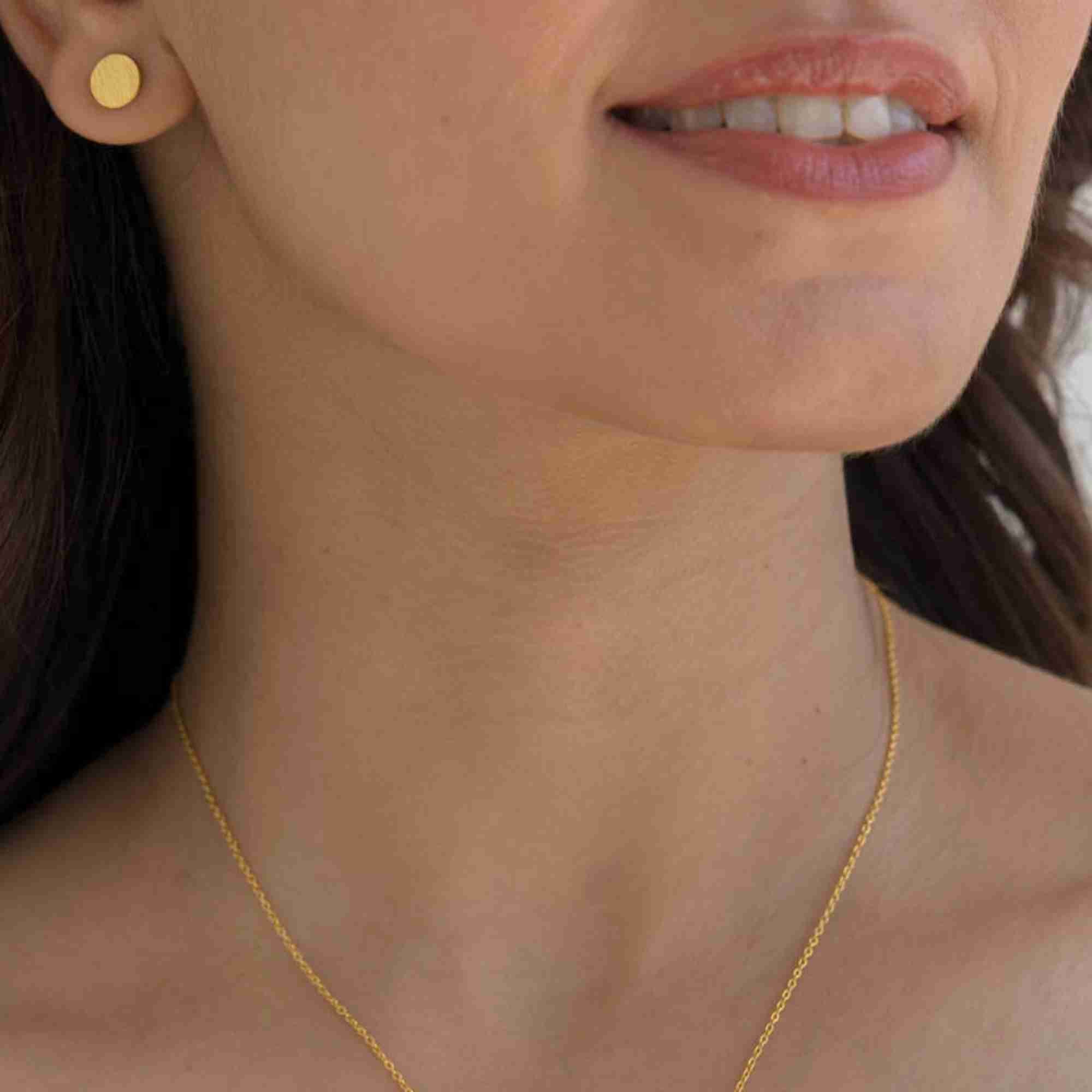 Cropped lifestyle view of a smiling model wearing the Shimmering Disks Minimalist Stud Earrings Gold, referencing file name Shimmering_Disks_71.jpg. The clean composition highlights the subtle shimmer and minimalist appeal of the round gold coin stud earring on her earlobe.