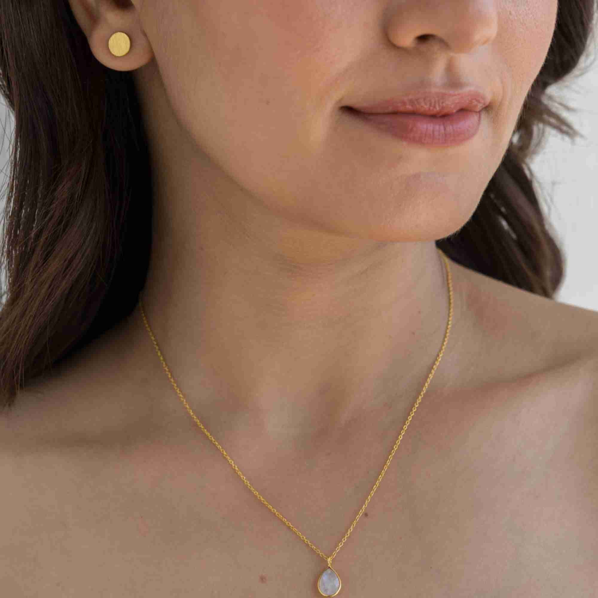 Lifestyle portrait of a model showcasing the Shimmering Disks Minimalist Stud Earrings Gold, referencing file name Shimmering_Disks_72.jpg. The shot shows her right profile with a small, flat yellow gold disc stud earring, beautifully paired with a delicate gold chain pendant necklace.